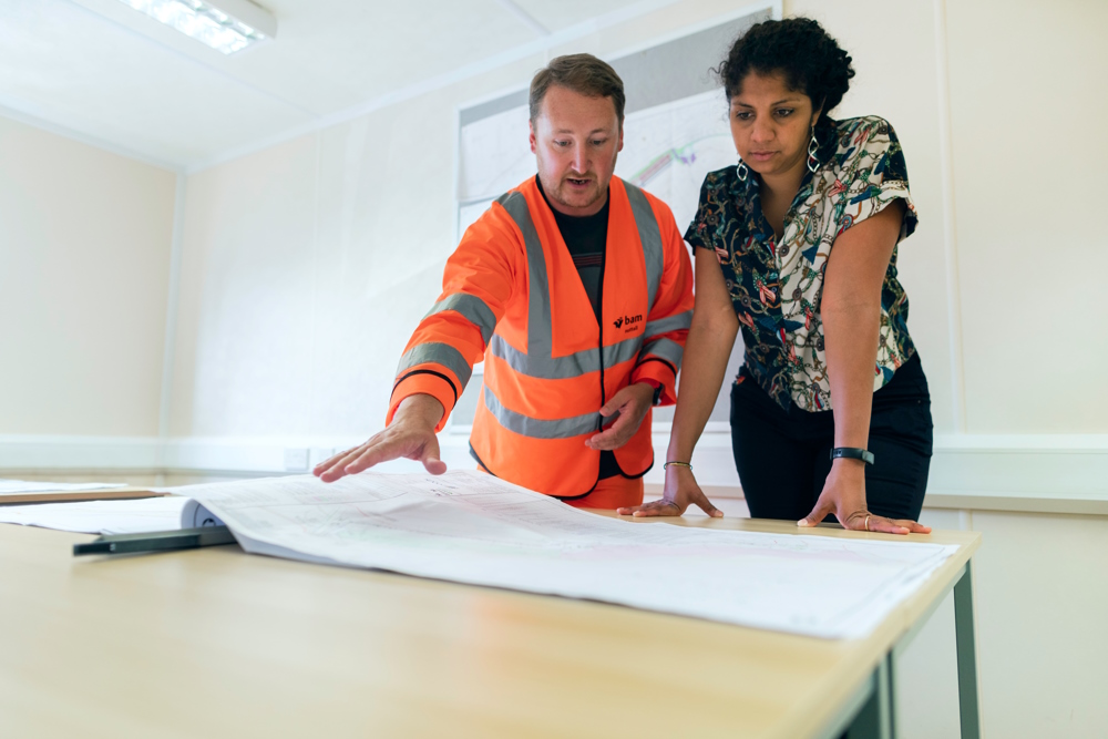 A man in a hi-vis jacket and a woman look over plans.
