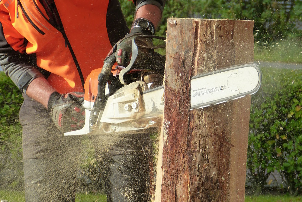 Man using a chainsaw on a tree stump.